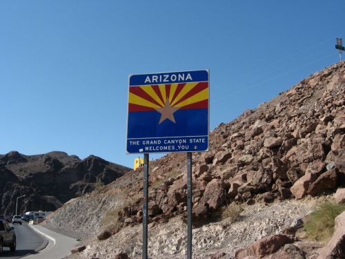 Sign welcoming visitors to Arizona, featuring the state flag design and the text "The Grand Canyon State Welcomes You."