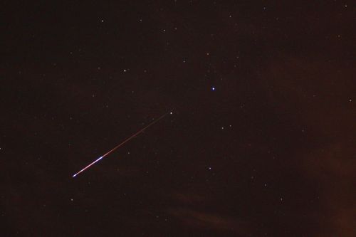 A bright meteor streaks across a starry night sky, leaving a glowing trail behind it.