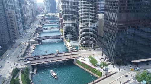 Aerial view of a city river with bridges, boats, and tall buildings lining the banks in an urban setting.