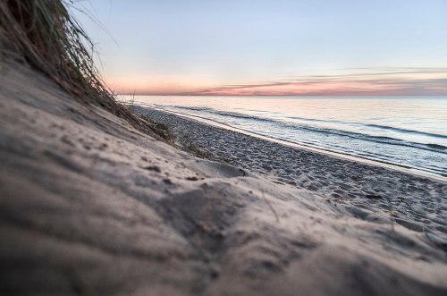 A serene beach at sunset, with gentle waves lapping at the shore and soft sand dunes in the foreground.