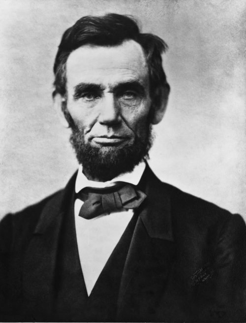 Black and white portrait of a man with a beard, wearing a suit and bow tie, looking directly at the camera.