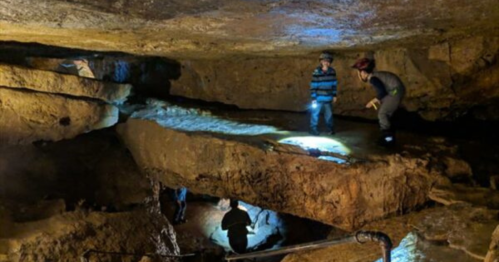 Explorers in a cave, using flashlights to navigate rocky terrain and illuminated areas.