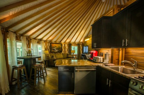 Cozy interior of a yurt featuring a kitchen, dining area, and living space with wooden beams and large windows.