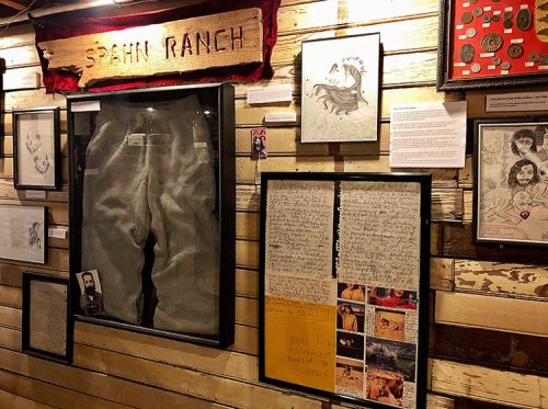 A wall display featuring framed art, letters, and a pair of jeans labeled "Spain Ranch."