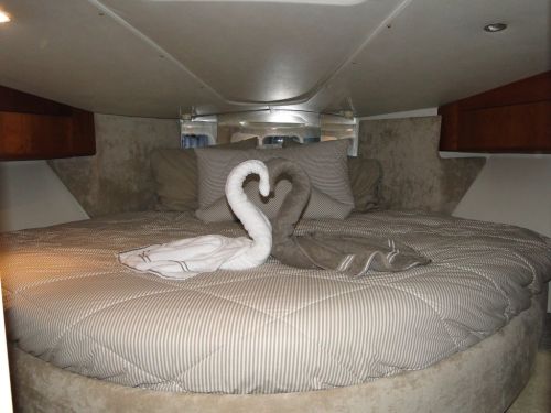 A cozy boat cabin with a round bed, featuring decorative towel swans and soft bedding in neutral tones.