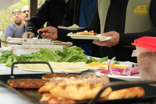 A buffet table with various foods, including salads, meats, and cheeses, as people serve themselves in the background.