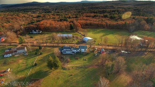 Aerial view of a rural landscape with houses, fields, and autumn foliage in the background.