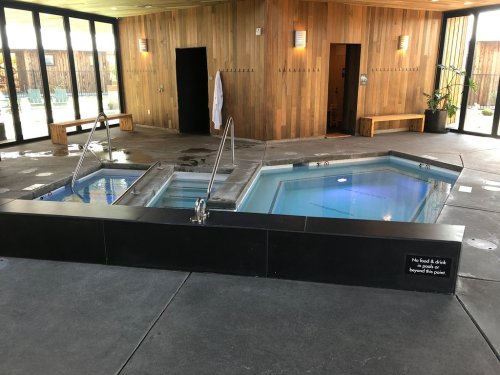 A modern spa area featuring two hot tubs, wooden walls, and a sign about food and drink restrictions.