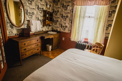 Cozy bedroom with a wooden dresser, sink, and vintage wallpaper, featuring a window with natural light.