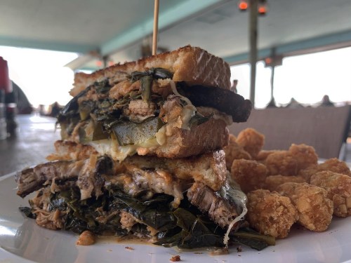 A towering sandwich filled with greens and meat, served with crispy tater tots on the side.