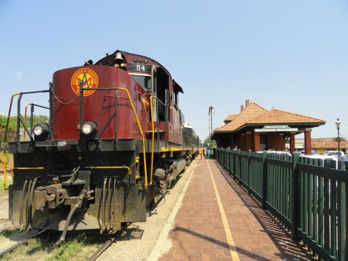 A vintage train at a station, with a red locomotive and a brick platform under a clear blue sky.