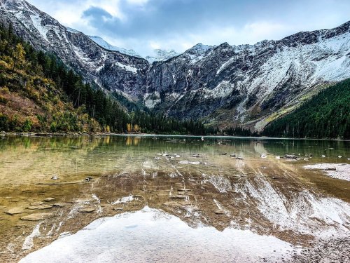 A serene mountain lake reflecting snow-capped peaks and lush forests under a cloudy sky.