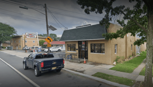 A brick building on a street corner with a pickup truck parked outside and a sign for a nearby pizza place.