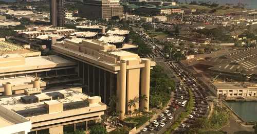 Aerial view of a busy urban area with a long line of cars on a road and buildings in the background.