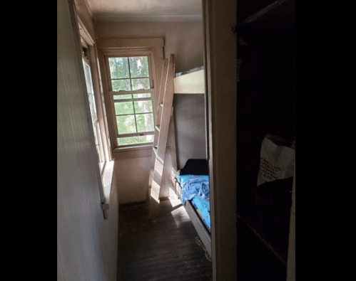 A small room with a bunk bed, a ladder, and a window showing greenery outside.