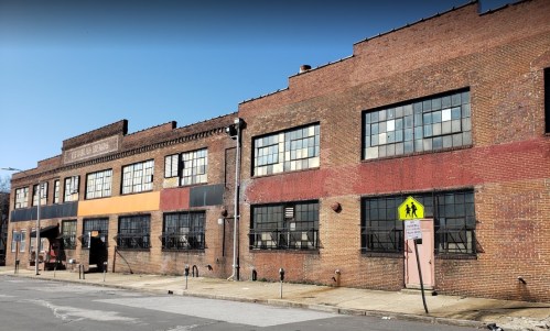 A brick building with large windows and colorful accents, featuring a crosswalk sign in front on a clear day.