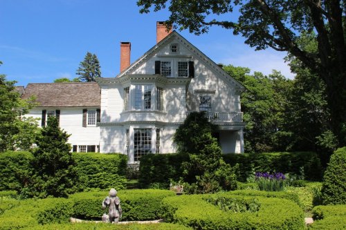 A large white house surrounded by lush greenery and a well-maintained garden under a clear blue sky.