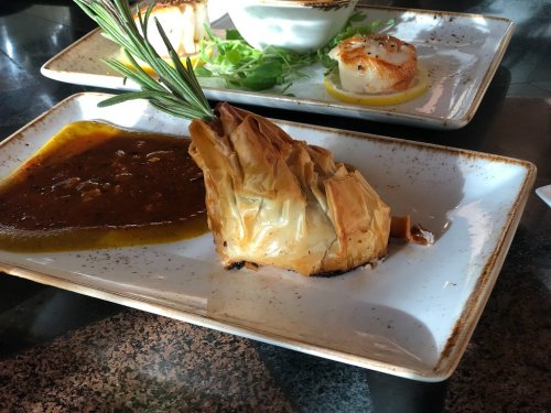A flaky pastry filled with savory ingredients, served on a plate with a rich sauce and garnished with herbs.