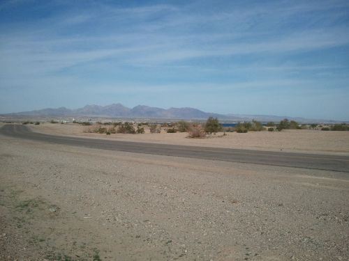 A wide view of a desert landscape with mountains in the background and a clear blue sky. A road runs through the scene.
