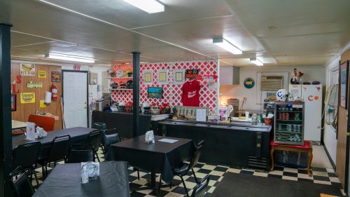A cozy diner interior with black and white checkered floors, tables, and a red and white patterned wall behind the counter.