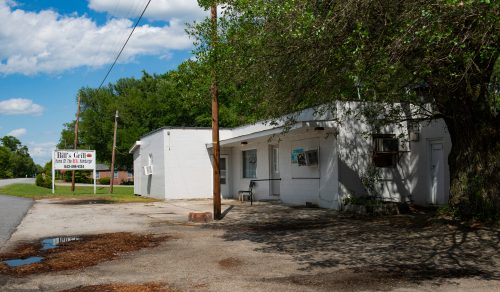 A small, white building with a sign for "Rita's Grillo," surrounded by greenery and a clear blue sky.