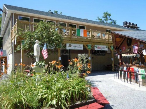 A rustic building with a balcony, decorated with flags and signs, surrounded by flowers and gravel pathways.