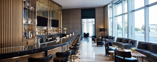 Modern bar interior with a sleek black countertop, stylish seating, and large windows letting in natural light.