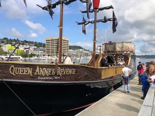 A pirate ship named "Queen Anne's Revenge" docked in Seattle, with people boarding and enjoying the waterfront view.