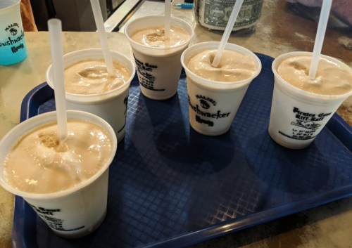 Six cups of frozen drinks with straws on a blue tray, set on a table.
