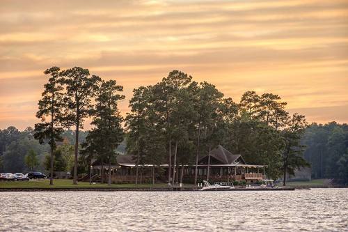 A serene lakeside view at sunset, featuring a building surrounded by trees and boats docked nearby.