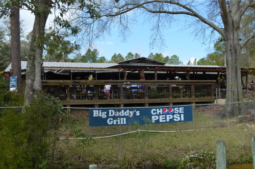 A rustic restaurant named Big Daddy's Grill with outdoor seating, surrounded by trees and a Choose Pepsi sign.