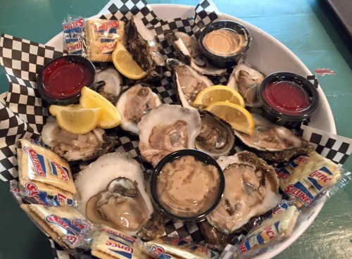 A platter of fresh oysters with lemon wedges and dipping sauces, served on a checkered paper.