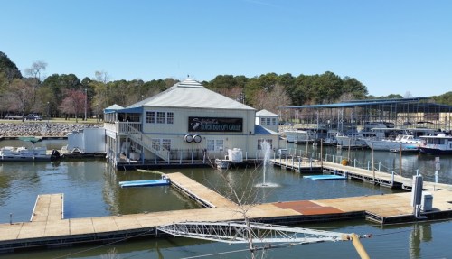 A marina with a large building labeled "Fish Dock Gallery" and several boats docked in calm waters under a clear blue sky.