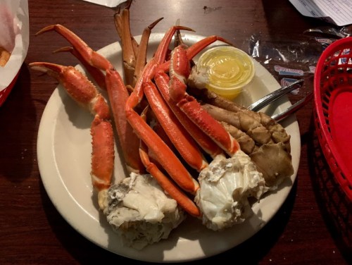 A plate of crab legs and claws, accompanied by a small container of dipping sauce.