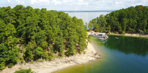 Aerial view of a serene lake surrounded by lush green trees and a small boat docked near the shore.