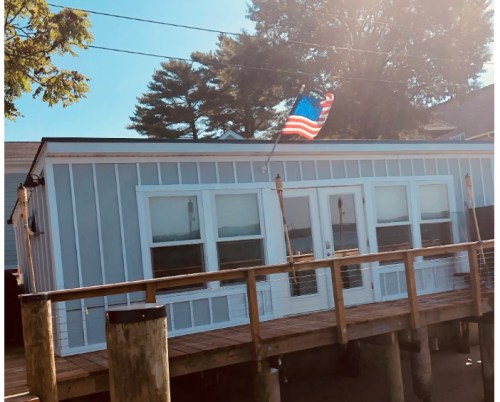 A light blue beach house with a wooden deck and an American flag waving in the breeze.