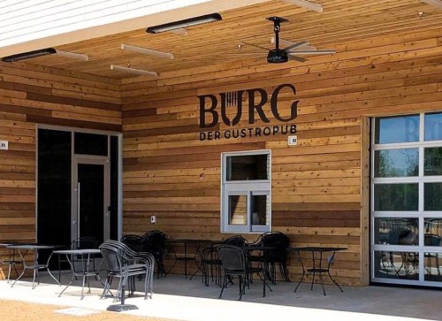 Exterior of a wooden building featuring the sign "BURG DER GUSTROPUB" and outdoor seating.