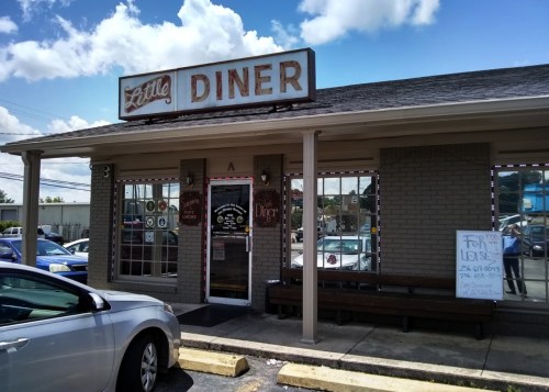 A small diner with a vintage sign, featuring large windows and a "For Lease" sign in front. Cars parked outside.