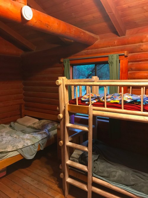 Cozy wooden cabin interior featuring a bunk bed and a single bed, with warm lighting and rustic decor.