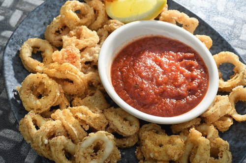A plate of crispy fried calamari rings served with marinara sauce and a lemon wedge.