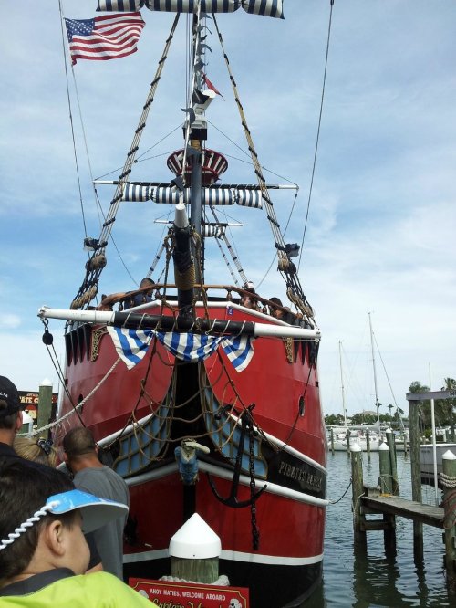 A large red pirate ship docked at a marina, with people on board and American flags flying.
