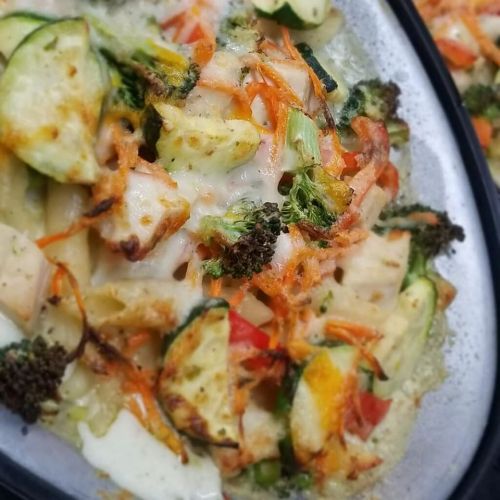 Sizzling dish with mixed vegetables, chicken, and melted cheese on a hot plate.