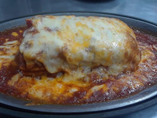 A cheesy lasagna topped with melted cheese, served in a rich tomato sauce on a black plate.