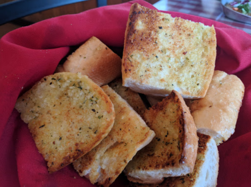 A basket filled with golden-brown garlic bread slices on a red cloth.