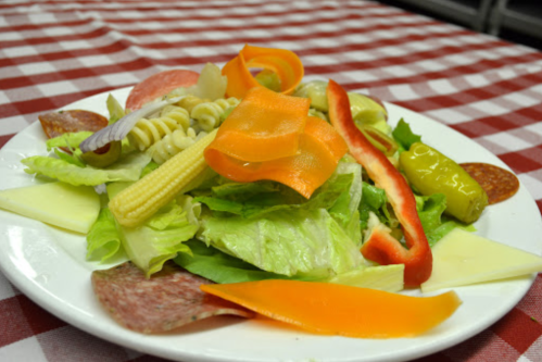 A colorful salad with lettuce, pasta, bell peppers, carrots, cheese, and assorted meats on a white plate.