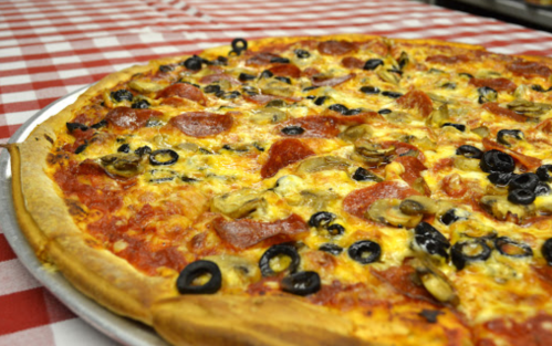 A large pizza topped with pepperoni, olives, and mushrooms on a red and white checkered tablecloth.
