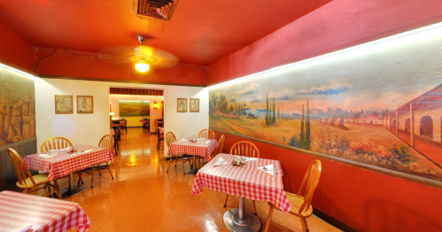 Cozy restaurant interior with red walls, checkered tablecloths, and scenic murals. Warm, inviting atmosphere.