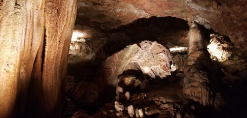 A dimly lit cave interior featuring rock formations and stalactites, with textured walls and scattered stones.