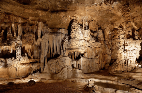 Stalactites and stalagmites in a dimly lit cave, showcasing intricate rock formations and textures.