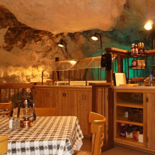 Cozy cave restaurant with wooden furniture, a checkered tablecloth, and a well-stocked counter under soft lighting.